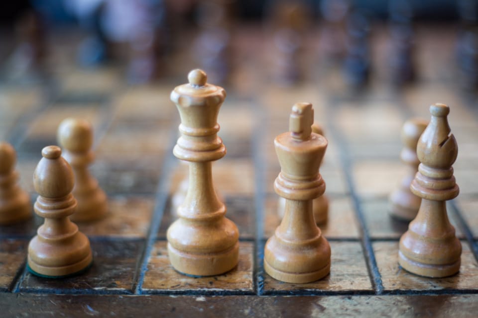 Wooden chess pieces standing on a worn playing board.