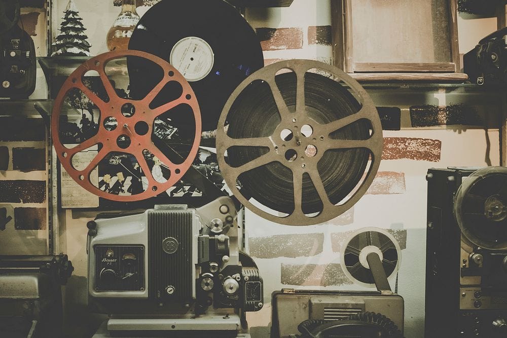 Vintage film reels and an old cine projector arranged against a poster-covered wall.